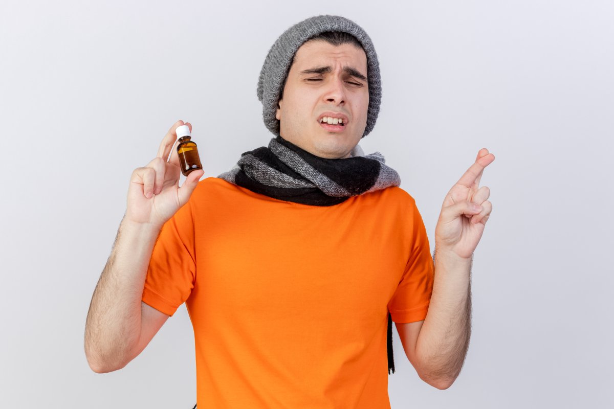 with-closed-eyes-concerned-young-ill-man-wearing-winter-hat-with-scarf-holding-medicine-glass (1)